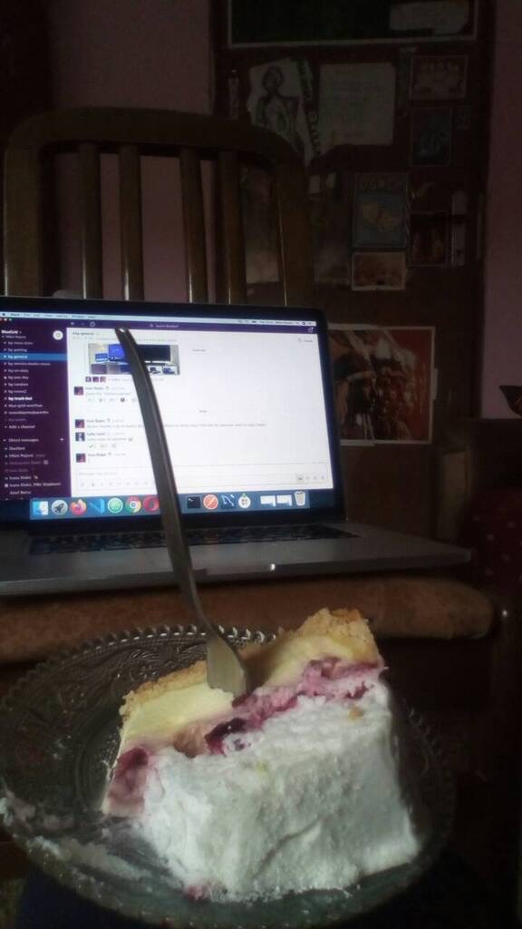 A home office desk setup for remote work with a piece of cake in the foreground.