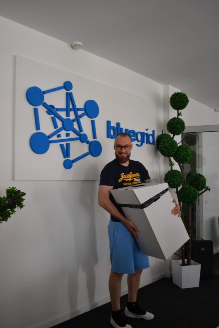 A man is smiling and holding a cardboard box in front of the BlueGrid logo.
