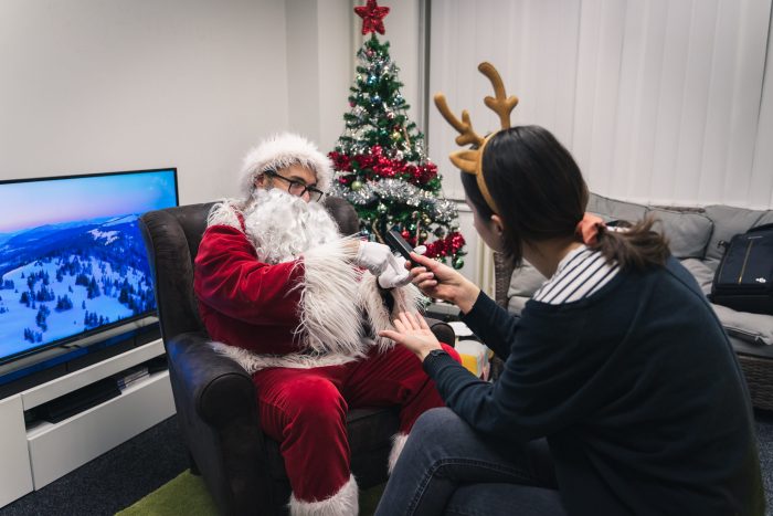A woman in a reindeer costume interviewing a man in a Santa costume next to a Christmas tree.