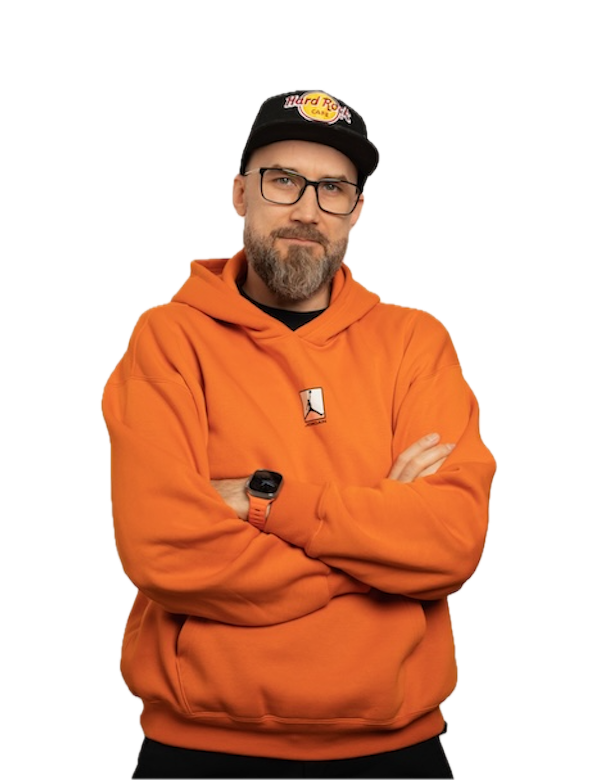 A man with a beard and glasses, wearing an orange hoodie and a black cap with a Hard Rock Cafe logo, stands with his arms crossed against a plain white background.