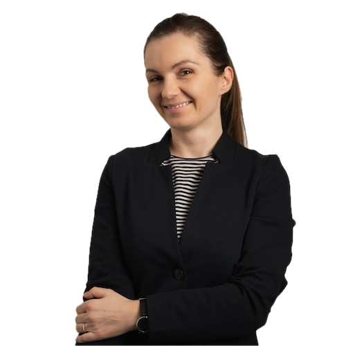 A woman with brown hair in a ponytail, wearing a black blazer over a striped shirt, smiles with her arms crossed against a plain white background.
